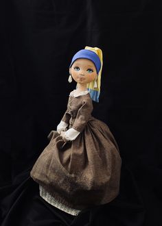 a doll wearing a brown dress and blue headband sitting on a black cloth background