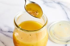 a spoon full of liquid sitting on top of a glass jar filled with honey syrup