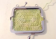 a green crocheted dishcloth hanging from a metal hook on a white wall