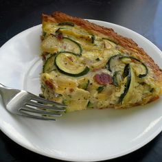 a slice of quiche with zucchini and bacon is on a white plate