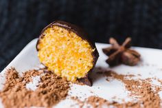 a piece of chocolate covered in yellow and white frosting next to some cocoa powder