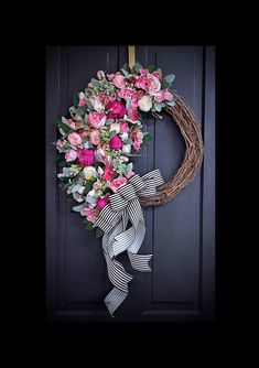 a wreath is hanging on the front door with pink flowers and ribbons around it,