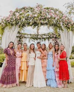 a group of women standing next to each other under a floral covered arch at a wedding