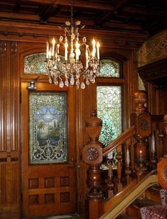 a chandelier hanging from the side of a wooden staircase in front of a stained glass door