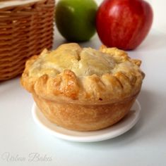 an apple pie sitting on top of a white plate next to two green and red apples