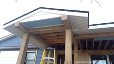 a house being built with wooden beams and sidings on the front porch, next to a ladder