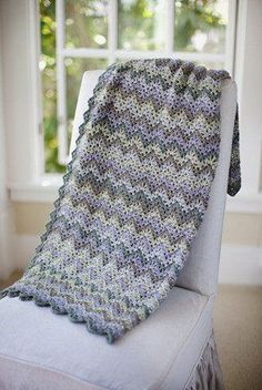 a crocheted blanket sitting on top of a white chair next to a window