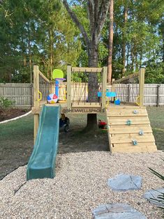 a playground with a slide and climbing wall in the back yard, next to a tree