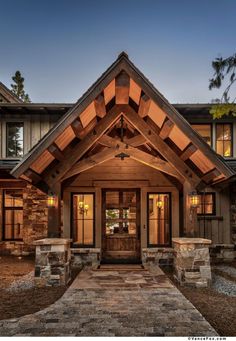 the front entrance to a home with stone pillars and wood trimmings, lit up at night