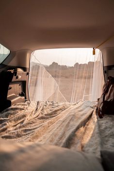 the interior of a vehicle with sheer curtains on it's windows and bed in the back