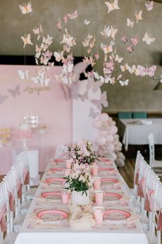 a table set up for a party with pink and white decorations hanging from the ceiling