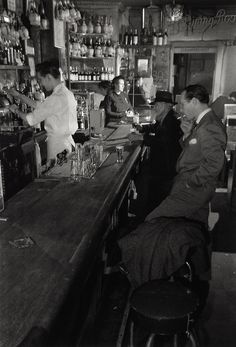 black and white photograph of men sitting at the bar in a restaurant with bartenders