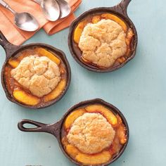 four cast iron skillets filled with peach cobbles on top of a blue table