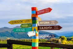 a pole with many different colored street signs on it's sides and mountains in the background