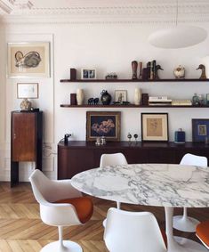 an elegant dining room with marble top table and white chairs in front of open shelves