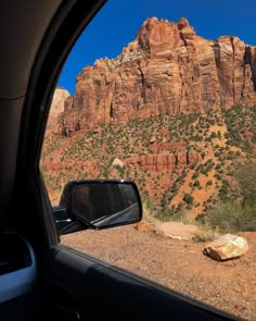 the view from inside a car looking at mountains and trees in the distance with a rock out front