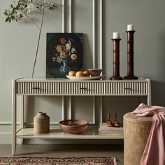 a white table with vases and fruit on it in front of a gray wall