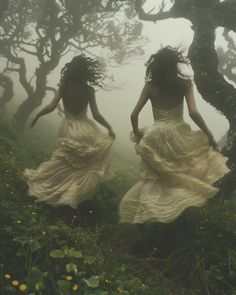 two women in white dresses are walking through the woods on a foggy, misty day