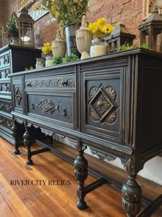 an old dresser is painted black and has flowers on the top, along with potted plants