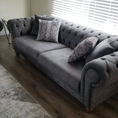 a grey couch sitting in front of a window with two pillows on top of it