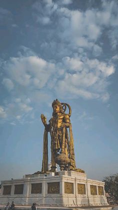 a large golden statue sitting in the middle of a park under a cloudy blue sky