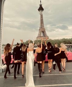 a group of women standing in front of the eiffel tower, with their arms raised