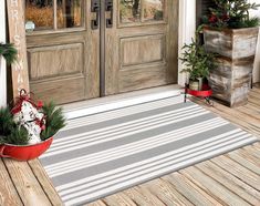 two potted plants sitting on the front porch next to a door with christmas decorations