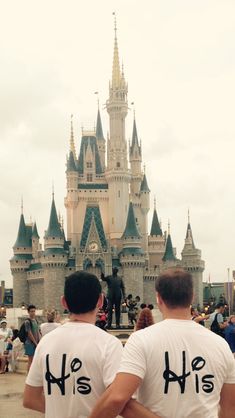 two men wearing white shirts with black letters on their backs in front of a castle