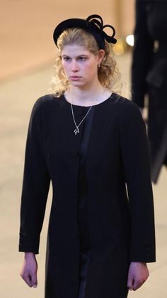 a woman with blonde hair wearing a black dress and hat walking down the street in front of other people