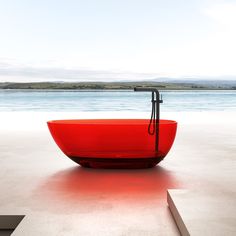 a red bathtub sitting on top of a cement floor next to the ocean with an umbrella