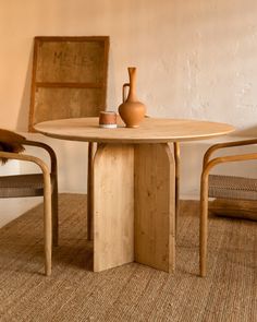 a wooden table with a vase on top and two chairs around it in front of a wall