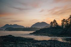 the sun is setting over some mountains and trees on the shore with water in front of them