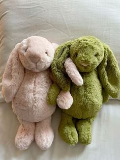 two stuffed animals sitting on top of a bed next to each other, one green and the other pink