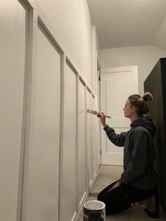 a woman is painting the wall with white paint