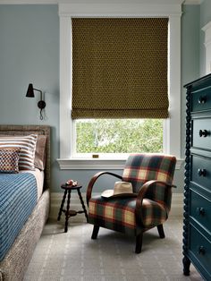 a plaid chair sits in front of a window with roman shades on the windowsill