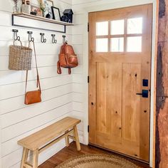 a wooden bench sitting in front of a door next to a wall with hooks on it