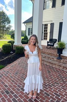 a woman standing on a brick walkway holding a drink