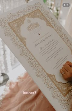 a person holding up a large white paper with gold trim and writing on the bottom