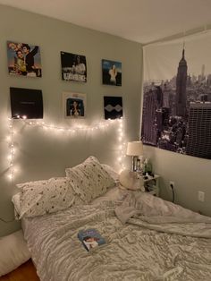 an unmade bed with white sheets and lights on the headboard is in front of a cityscape