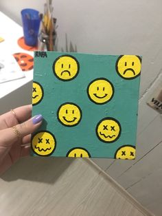 a person holding up a small piece of paper with smiley faces painted on it in front of a table