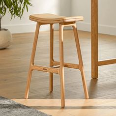 a wooden stool sitting on top of a hard wood floor next to a potted plant