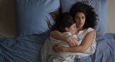 two women hugging each other on a bed with blue sheets and pillows in the background