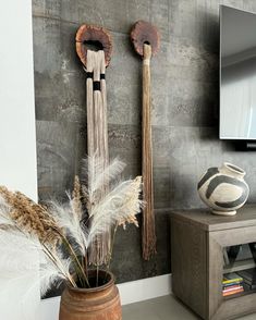 two decorative objects are hanging on the wall next to a vase with feathers in it