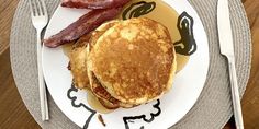 a plate with pancakes and bacon on it next to a fork, knife and spoon