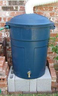 a large blue trash can sitting next to a brick wall with a hose connected to it