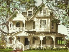 an old victorian house is painted white and has flowers in the front yard, along with some trees