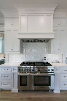 a large kitchen with white cabinets and stainless steel stove top oven, range hood, and hardwood flooring