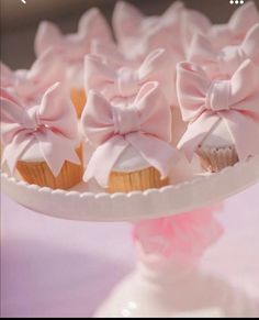 cupcakes with pink bows are on a cake plate in front of other cupcakes