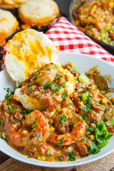 a bowl filled with shrimp and vegetables next to bread on a checkered table cloth