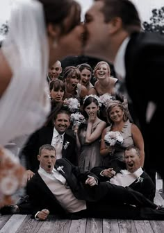 a bride and groom kissing in front of their wedding party on the dock at sunset